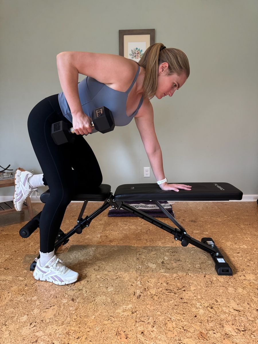 Sadie demonstrating a single-arm dumbbell row on a bench in her Black Mountain studio