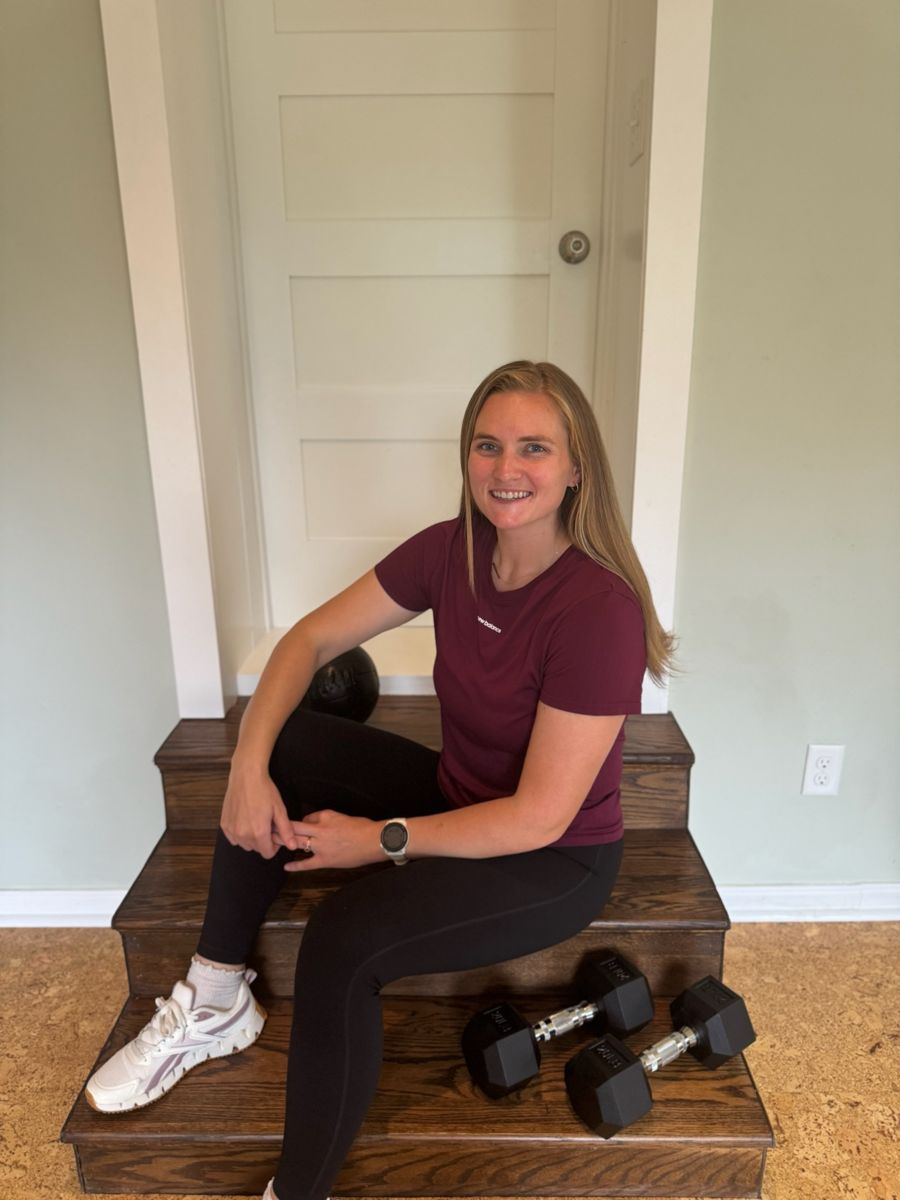 Sadie sitting on wooden studio steps beside a pair of dumbbells